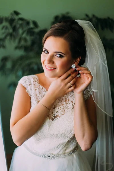 Elegante sposa alla ricerca vestirsi in abito bianco indossando gli orecchini, preparando per il matrimonio — Foto Stock