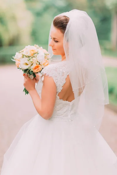 Il primo piano vista posteriore della sposa con le spalle nude che tengono il bouquet di nozze nel parco . — Foto Stock