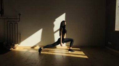 Athetic kız lunges poz duruyor, boyun tutarak ve geri hareket pencerenin yakınındaki.