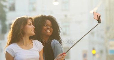 Düzülmüş kız selfie stick kullanarak fotoğraf çekmek tarafından eğleniyor. Onlardan biri Afro-Amerikan.