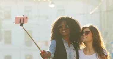 Güneş gözlüğü ile muhteşem gülümseyen kız sokakta yürürken selfie stick kullanarak çekim.