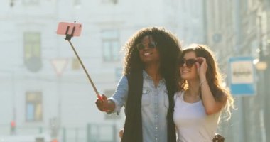 Yakın çekim yürüyüş sırasında selfie stick kullanarak fotoğraf çekerken işaret barış gösterilen güneş gözlüğü, düzeltme iki güzel gülümseyen kız portresi.