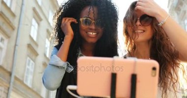 İki muhteşem gülümseyen kız saç düzeltme ve cep telefonu selfies çekerken sarılma. Onlardan biri Afro-Amerikan.