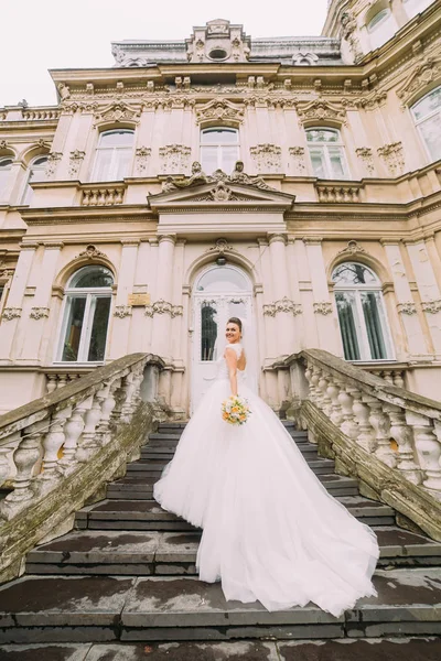 A noiva no vestido de casamento longo está segurando o buquê amarelo enquanto está de pé nas escadas do edifício austríaco . — Fotografia de Stock