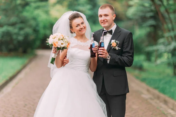The horizontal portrait of the smiling newlyweds holding the beverages. — Stock Photo, Image