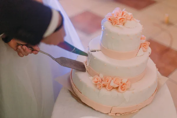 Die Nahaufnahme der frisch vermählten Hände beim Anschneiden des ersten Teils der Hochzeitstorte. — Stockfoto