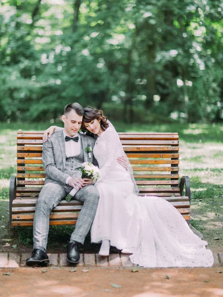 O retrato completo do feliz vintage recém-casados vestidos sentados no banco no parque . — Fotografia de Stock