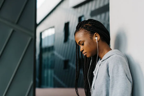 Adolescente afro-americano cuidadoso nos fones de ouvido que se apoiam na parede. Retrato lateral ao ar livre . — Fotografia de Stock