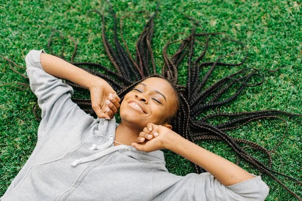 Retrato emocional de la alegre mujer afroamericana moviendo las manos mientras yacía sobre la hierba y escuchaba música . — Foto de Stock