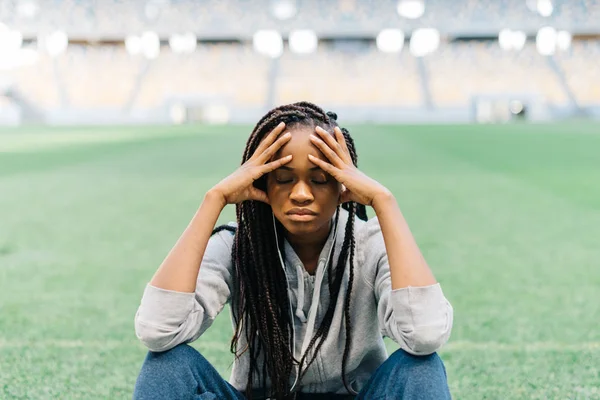 Retrato de cerca de la deportista afro-americana pensativa sentada en la hierba y apoyada en las rodillas . —  Fotos de Stock
