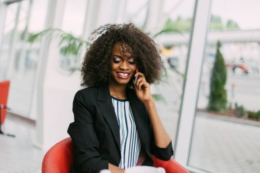 Neşeli Afro-Amerikan kadın kafede vakit ise cep telefonu aracılığıyla konuşuyor.