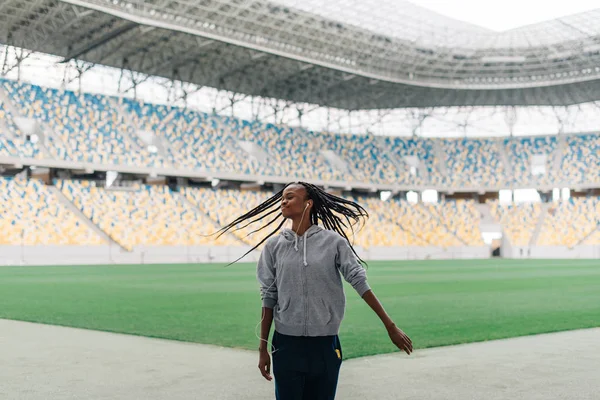 La encantadora deportista afro-americana en los auriculares está sacudiendo el pelo en el estadio . — Foto de Stock