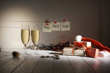 Yeni yıl iki kadeh şampanya, sarılmış hediyeler ve masaya döşeme çelenk bileşimi. İşareti yeni yıl ipe asılı.