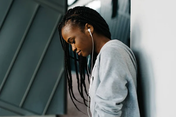 Retrato lateral de la joven afro-americana sonriente en los auriculares parados cerca de la pared . —  Fotos de Stock