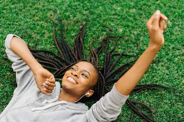 Πάνω από το πορτραίτο του χαρούμενη αφροαμερικάνικης εφήβου τοποθέτηση στο γρασίδι ενώ ακούτε μουσική και κίνηση τα χέρια. — Φωτογραφία Αρχείου