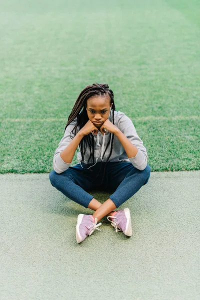 Over utsikten til den sørgelige afroamerikanske tenåringen som sitter på gresset og lener seg mot hendene . – stockfoto
