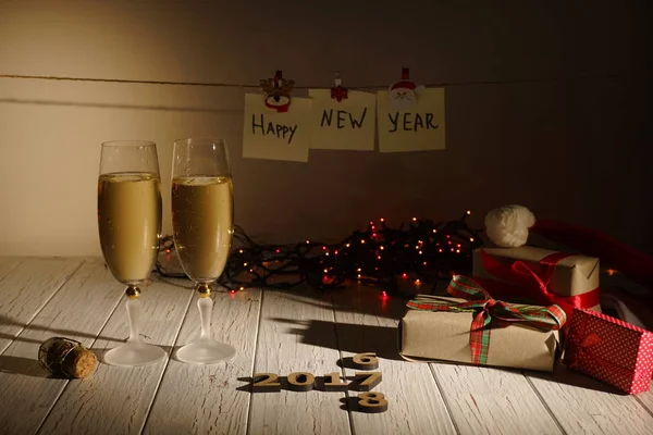 İki kadeh şampanya, sarılmış hediyeler, yeni yıl işareti ipe asılı ve çelenk aydınlatma Noel kompozisyon yatay görünüm.