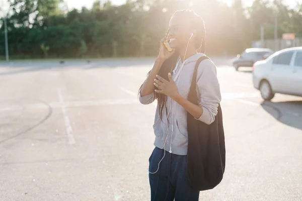 Feliz afro-americano adolescente está hablando a través del teléfono de venta durante la puesta del sol. El retrato al aire libre . — Foto de Stock