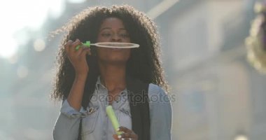 Yakın çekim yuvarlak iplik ise sabun köpüğü üfleme kıvırcık saçlı sevimli gülümseyen Afro-Amerikan kız portresi. Sokak konumu.