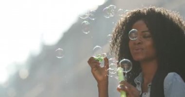 Kıvırcık saçlı oldukça Afro-Amerikan kız sabun köpüğü üfleme ve yuvarlak sunne sokak yürüyüş sırasında iplik. Yakın çekim portre.