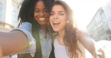 Gün batımı sırasında cadde boyunca yürürken komik surat güzel gülümseyen çok kültürlü girlfrineds duygusal selfie. Hızlı hareket.