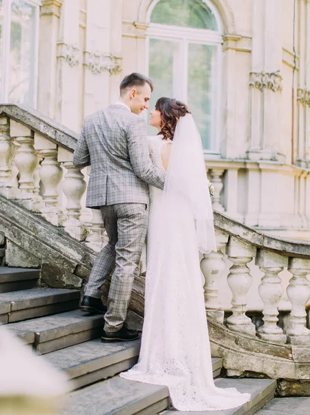 Le marié heureux étreint la mariée tout en se tenant debout dans les escaliers. La vue arrière . — Photo