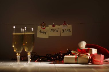 Mutlu yeni yıl işareti odak. Bardak şampanya, parlayan çelenk ve Noel hediyeleri bileşimi.