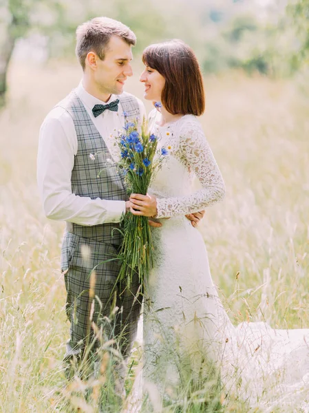 Το γκρο πλαν θέα στους ευτυχείς νεόνυμφους. Η νύφη κρατάει τα μπλε άγρια λουλούδια. — Φωτογραφία Αρχείου