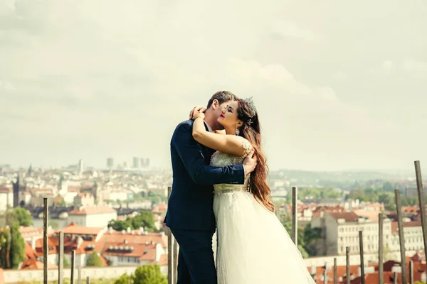 Retrato de meio-comprimento do casal recém-casado alegre abraçando no fundo do panorama de Praga . — Fotografia de Stock