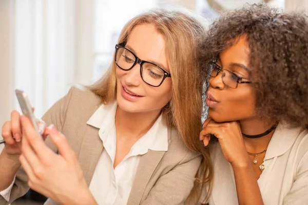 Dos mujeres sonrientes mirando el teléfono. Una de las mujeres es afroamericana . — Foto de Stock