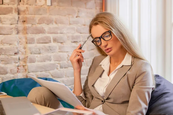 Σοβαρή επιχείρηση γυναίκα κάθεται με γραφικά ή χρονοδιαγράμματα στα χέρια της. Γυναίκα που φοράει γυαλιά και παλτό και φούστα. — Φωτογραφία Αρχείου