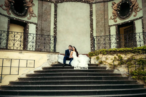 Das vertikale Foto des fröhlichen Brautpaares, das auf der Treppe des antiken Gebäudes in Prag sitzt. — Stockfoto