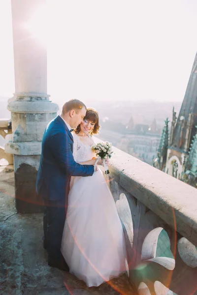 Bruid en bruidegom omhelzen elkaar op het balkon van de oude gotische kathedraal — Stockfoto