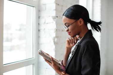 Pencerenin kenarında duran ve elleri tablet bakarak güzel afroamerican genç kız