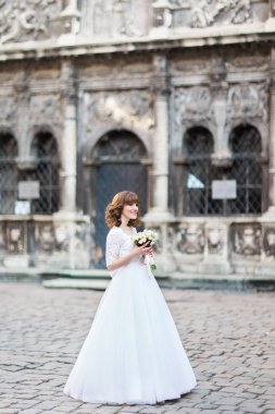 Gülümseyen gelin düğün buket sokakta tutarak tam uzunlukta yan görünüm.