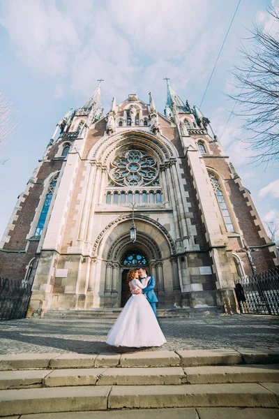 Newlyweds knuffelen in de voorkant van de kathedraal. — Stockfoto