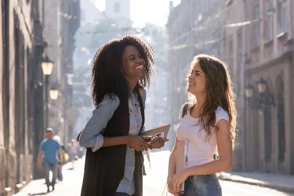 Lächelnde Freunde, die sich auf der Straße unterhielten. ein Mädchen ist schwarz mit langen lockigen Haaren. — Stockfoto