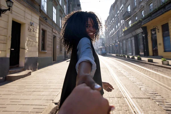 Atractiva chica negra sosteniendo la mano de un hombre o una mujer y sonriendo a la cámara . — Foto de Stock