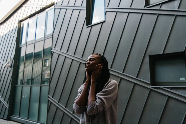 A jovem afro-americana está tendo prazer em ouvir música nos fones de ouvido. Retrato exterior . — Fotografia de Stock