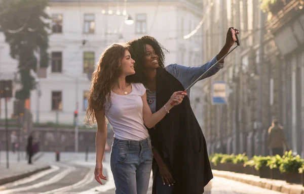 Dois jovens amigos andando nas ruas e fazendo selfie. preto menina e ela branco amigo . — Fotografia de Stock