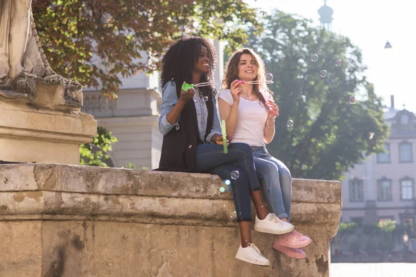 İki mutlu arkadaş sabun köpüğü ile eğleniyor. Anıtın merkezinde yakın oturan ve rahat kıyafetler giyen kızlar. Bir kız siyah.