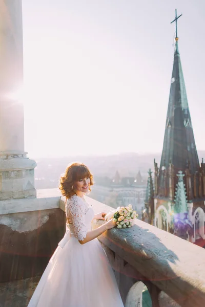 Elegante bruid poses op het balkon van de toren van antieke gotische kathedraal — Stockfoto