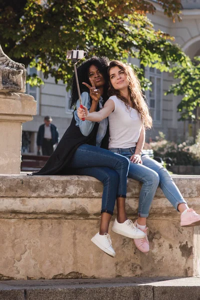 Zwei attraktive junge Mädchen machen ein Selfie in der Nähe des Denkmals in der Innenstadt. ein Mädchen ist schwarz. — Stockfoto