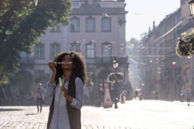 Kabarcıklar buz sokakta üfleme uzun kıvırcık saçlı güzel siyah kadın. Güneşli bir gün. Rahat yaşam tarzı kavramı.