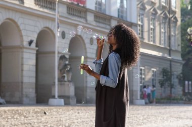 Afroamerican kabarcıklar sokakta üfleme uzun kıvırcık saçlı genç kadın. Rahat kıyafetler giyen kadın.