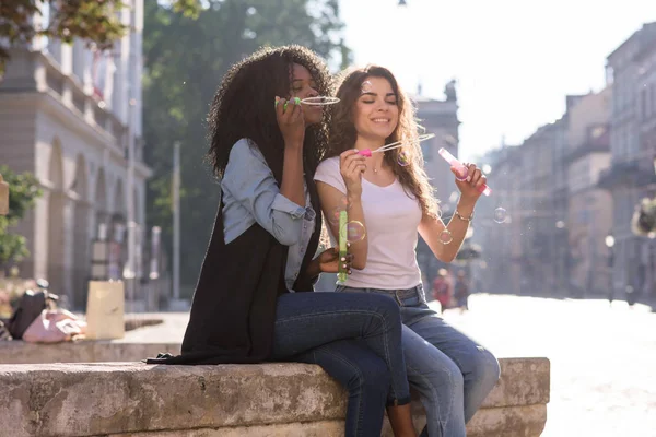 Zwei Freunde, die auf der Straße sitzen und Blasen blasen. schwarzes Mädchen mit ihrem Freund. — Stockfoto