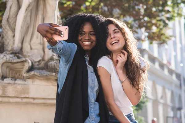 Glückliche Frauen, die Selfiewoman machen, stehen in der Nähe des Denkmals in der Innenstadt. schöne Architektur ringsum. ein Afroamerikaner mit dunklem lockigem Haar. — Stockfoto