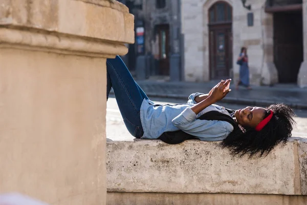 Eller güzel afroamerican kız lyingnear anıt tablet veya telefon ile er. Rahat kıyafetler giyen kız. — Stok fotoğraf