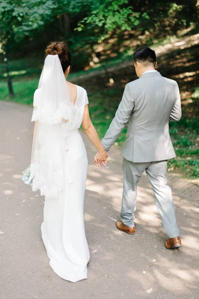 Groom em terno cinza segura a mão das noivas enquanto caminham no verão — Fotografia de Stock