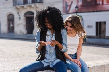 Şehir merkezinde oturan ve telefon ekranına bakarak iki çekici kız. Seyahat kavramı.